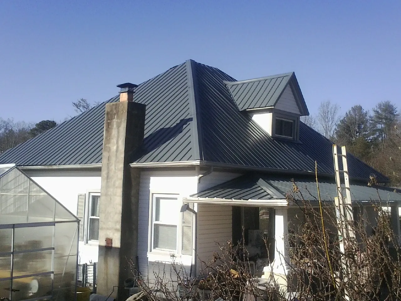 Dark blue standing seam metal roof on a white farmhouse with dormer — Slate & Tile Roof Repair by Roofing Brothers in Mc Kean