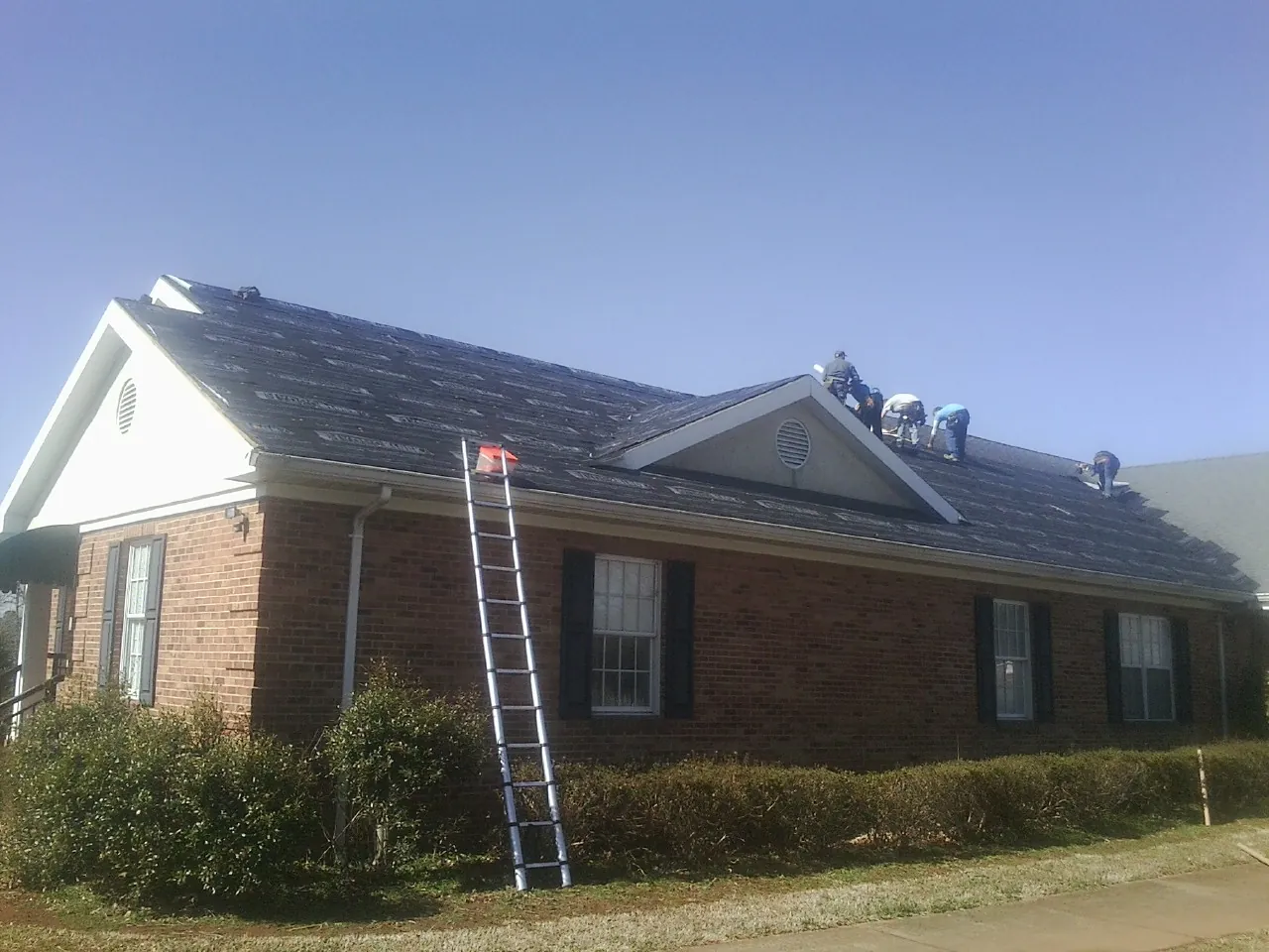 Crew tearing shingles off a brick ranch roof with a ladder set — Metal Roof Repair work by our crew in Mc Kean