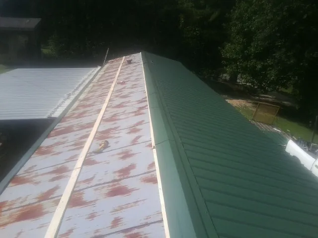 Old rusted panels beside newly installed green metal roofing — Wind Damage Roof Repair by Roofing Brothers in Mc Kean