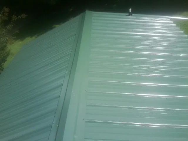 New green metal panels meeting at the ridge of a roof — Flat Roof Repair work by our crew in Mc Kean