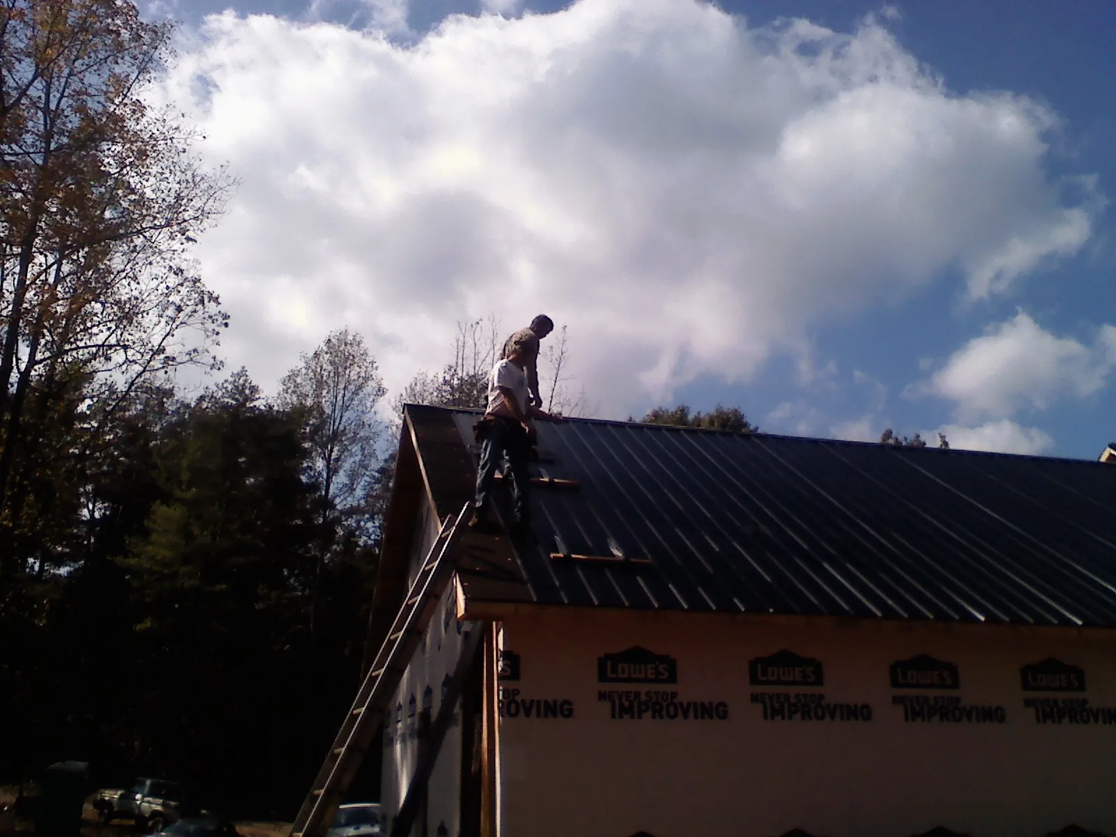 Roofer fastening dark metal panels high against a cloudy sky, from a Roof Inspection job in Mc Kean