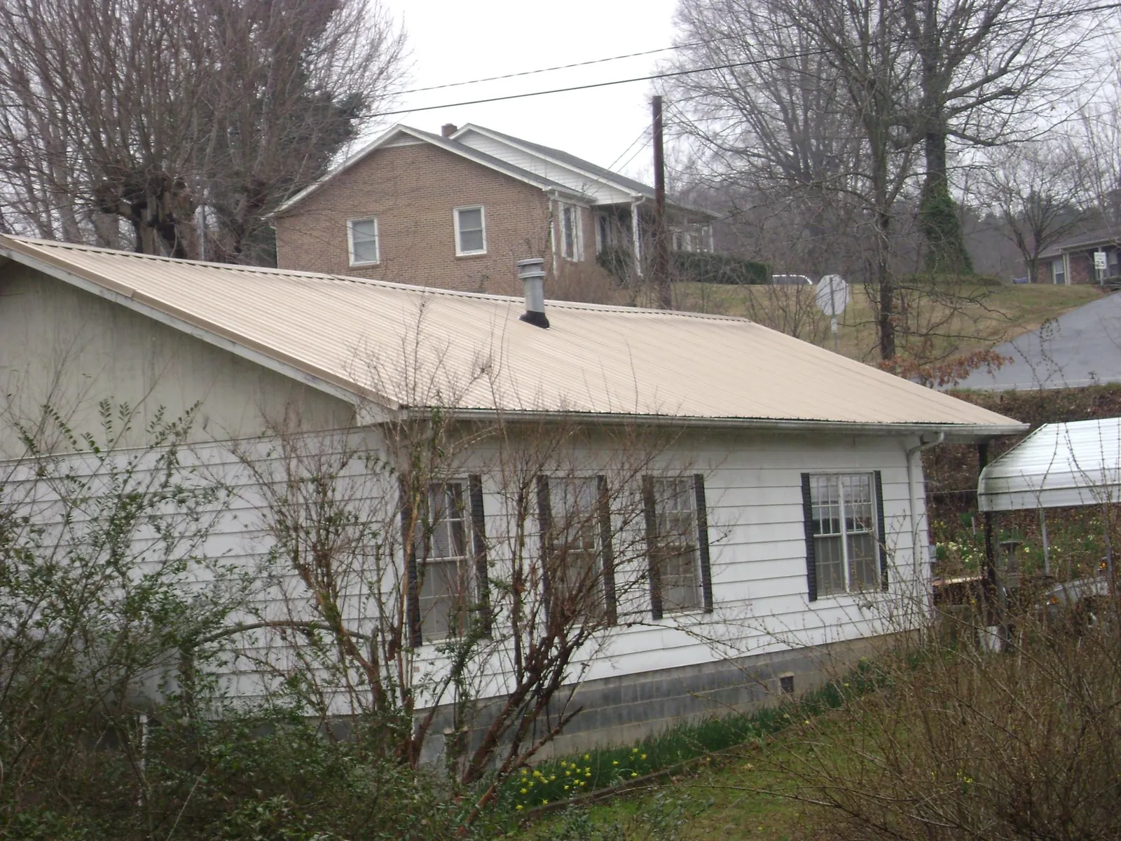 Tan metal roof on a white sided house set into a hillside — Commercial Roofing by Roofing Brothers in Mc Kean