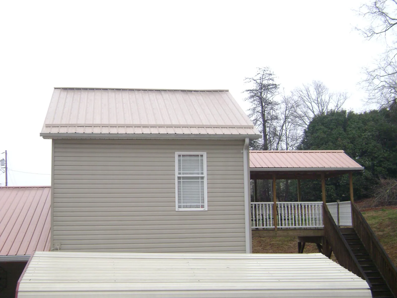 Tan metal roofs on a two story addition and attached porch, from a Roof Replacement job in Mc Kean